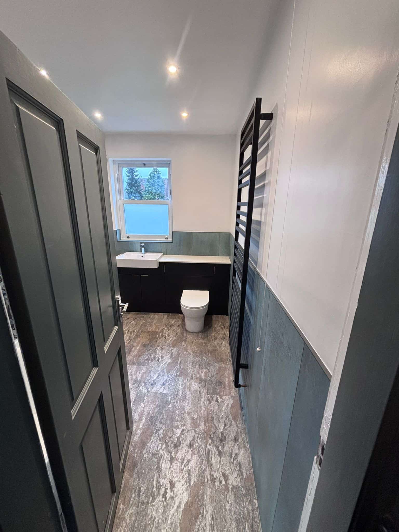 WC with a dark vanity, wall-hung basin, black towel rail and sage half-height tiling
