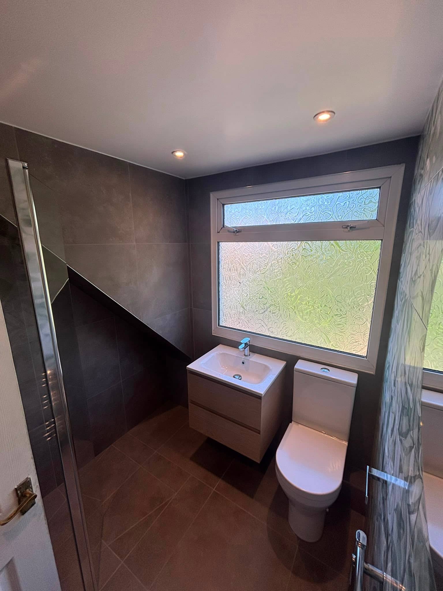 Compact loft bathroom with charcoal tiling, a wall-hung basin and a sloped ceiling