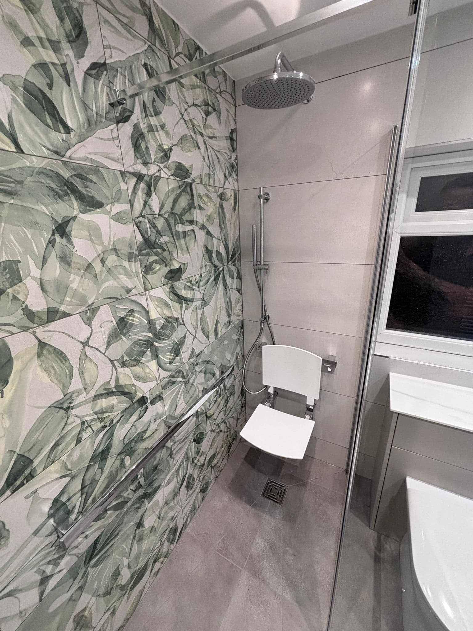 Accessible shower with a fold-down seat, grab rails and botanical feature tiling