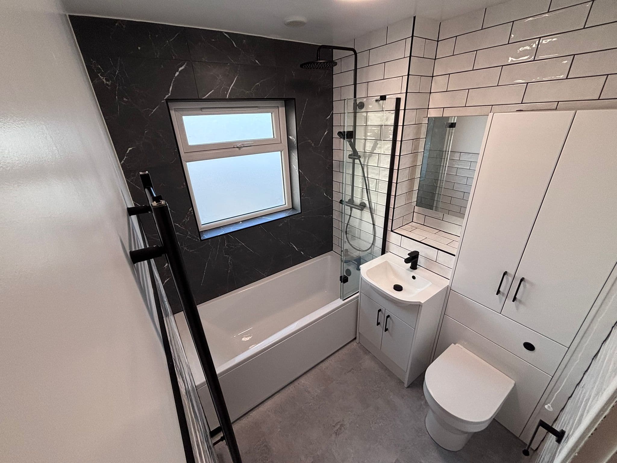 Family bathroom with a black marble feature wall, white metro tiling and a shower over the bath