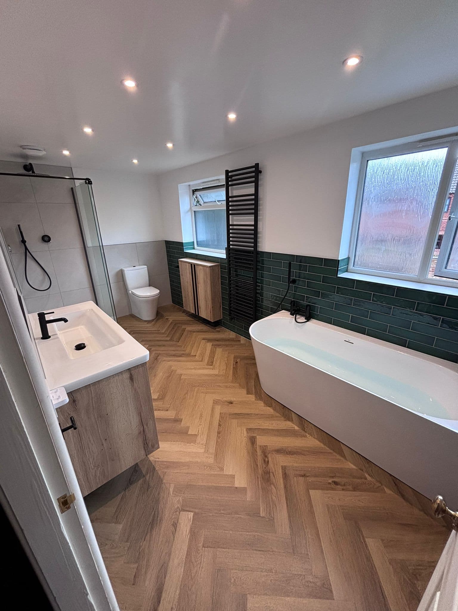 Finished bathroom with a back-to-wall bath, walk-in glass shower, oak vanity and green tiled band, supplied and fitted by Goldswan