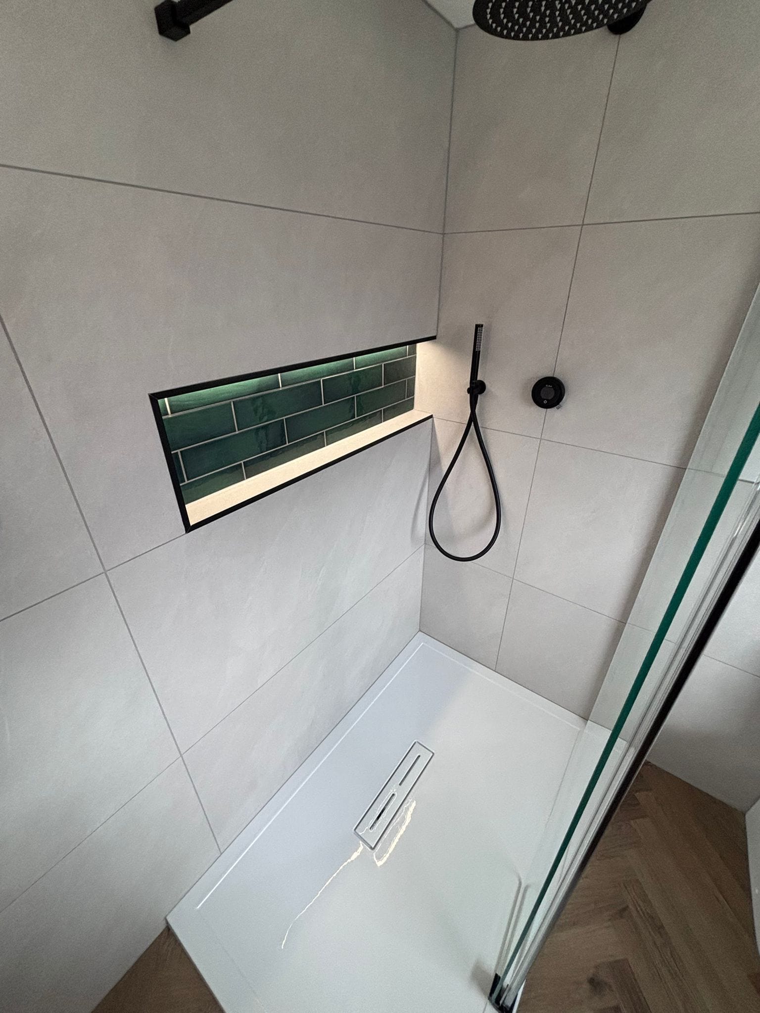 Black rainfall shower beside a green tiled niche with LED strip lighting