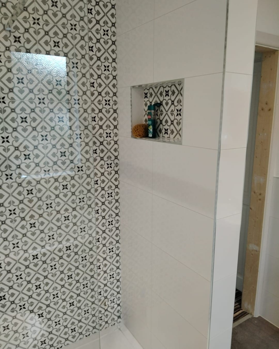 Recessed tiled shelf set into the shower wall, where the patterned tiles meet the plain white ones