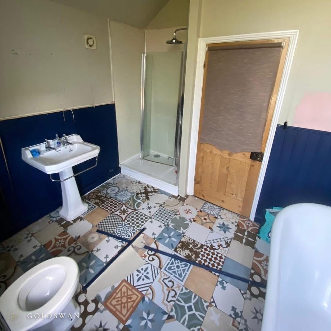 The bathroom before: navy tongue and groove panelling, a pedestal basin, a corner shower and a patchwork of patterned floor tiles