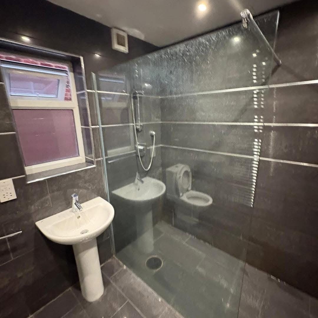 The old shower enclosure before the work, with a raised tray and dark grey tiling throughout