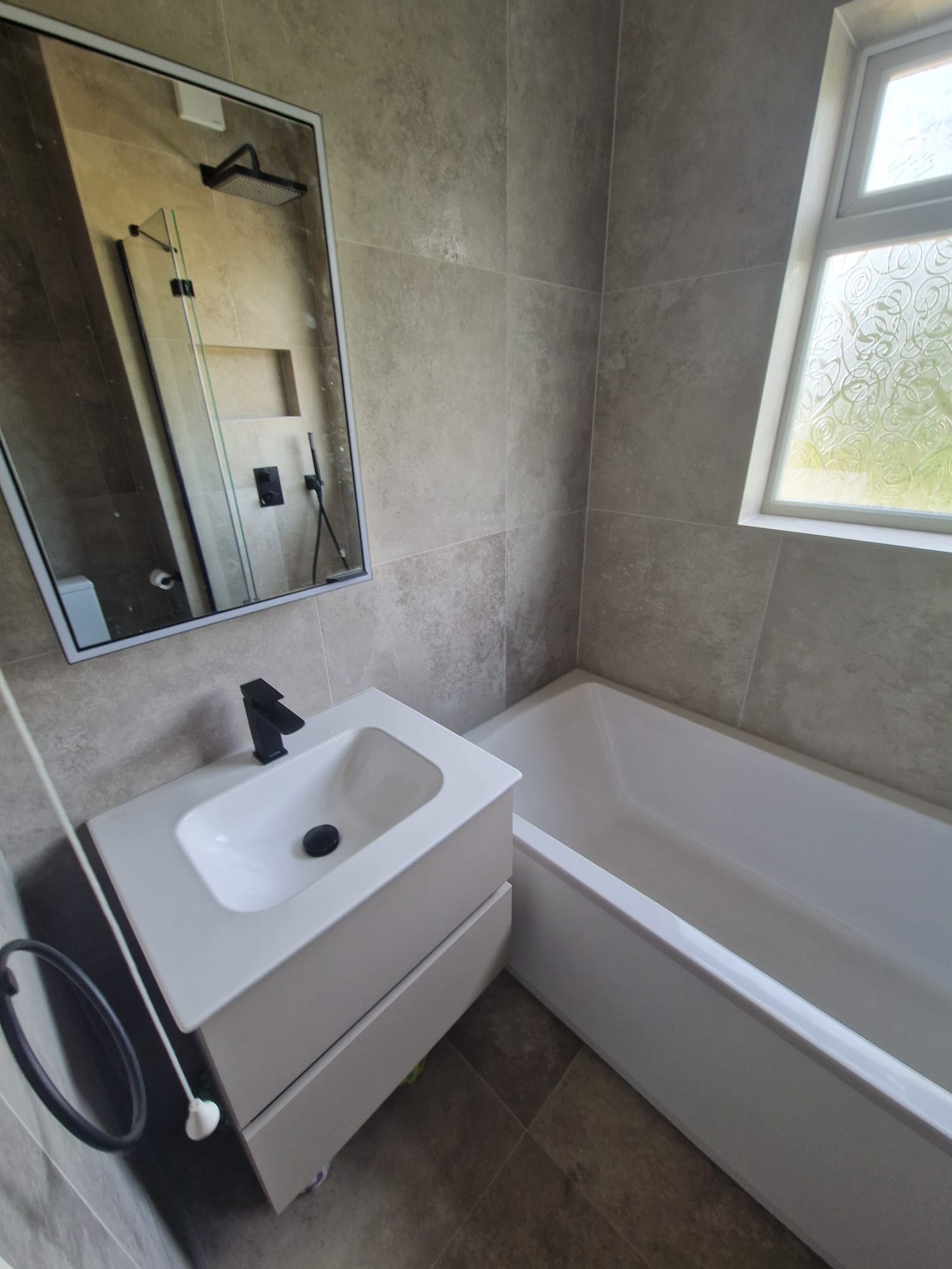 Wall hung vanity unit with a black tap and a black framed mirror, next to the bath