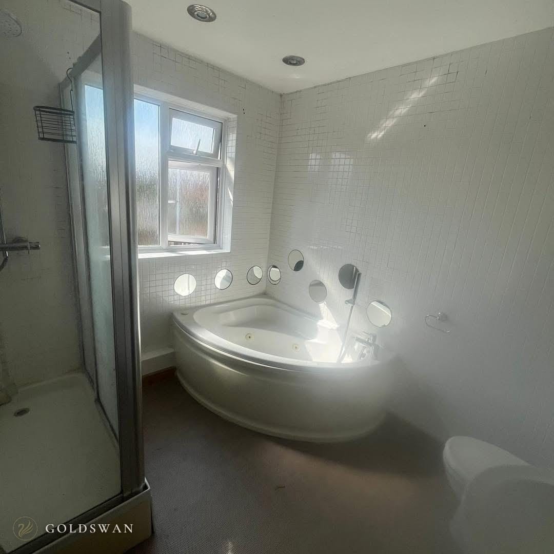 The bathroom before: a corner whirlpool bath with small round mirrors set into white mosaic tile, beside a shower cubicle