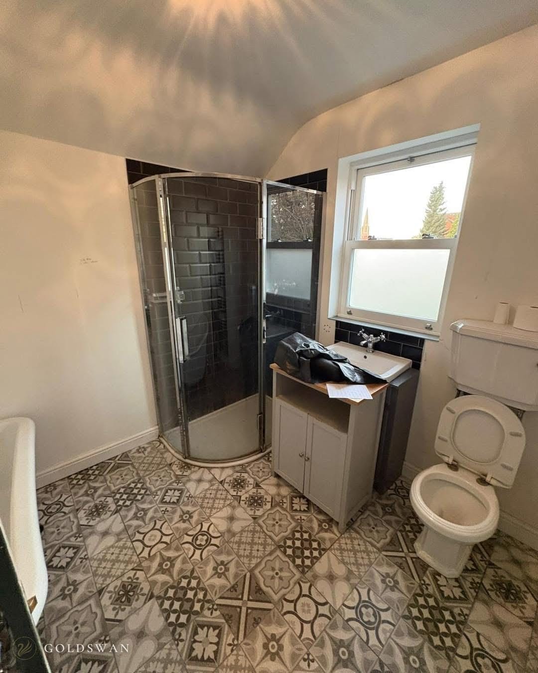 The bathroom before: a quadrant shower lined in black metro tile, a basin on a grey freestanding cabinet and a close coupled WC