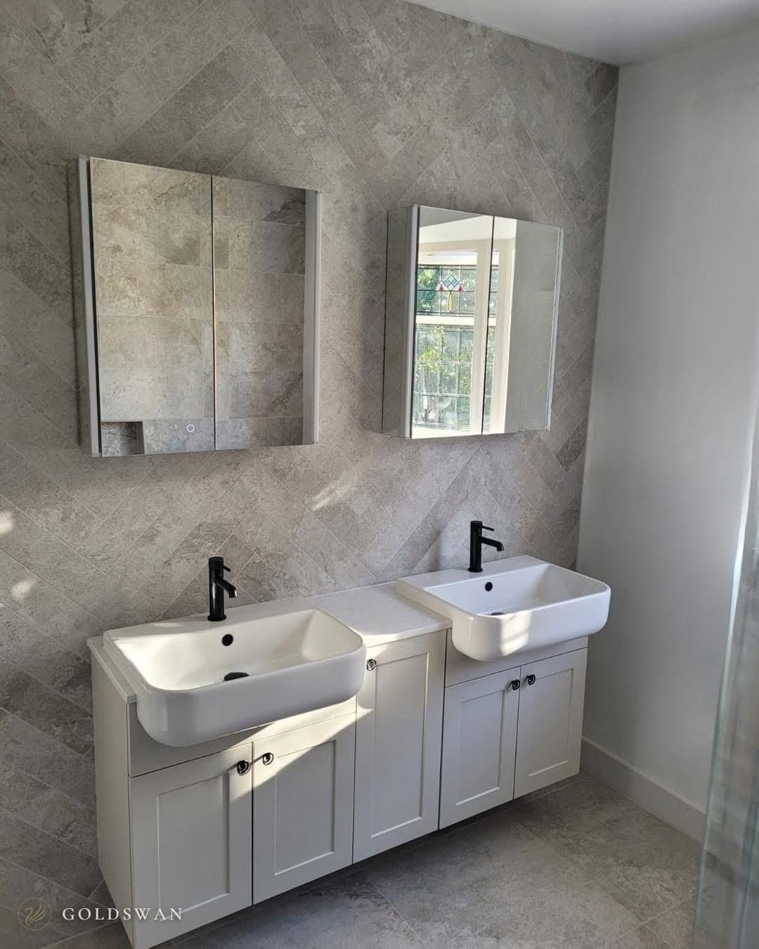 Two semi-recessed basins with matt black taps on pale shaker style units, under two mirror cabinets on grey stone effect tile laid in herringbone