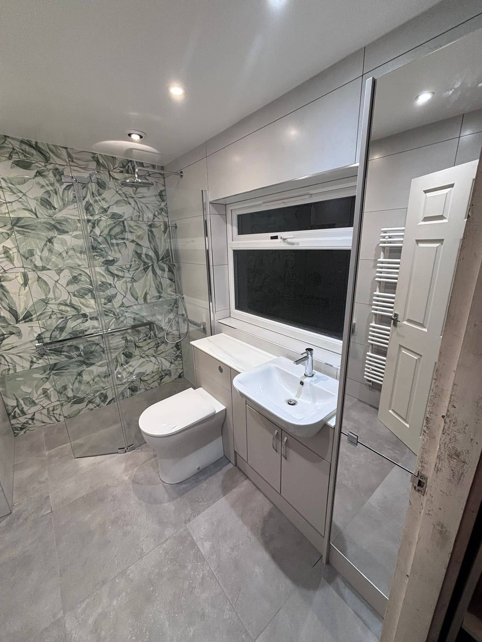 Wet room with botanical shower tiles, wall-hung toilet and marble-topped vanity