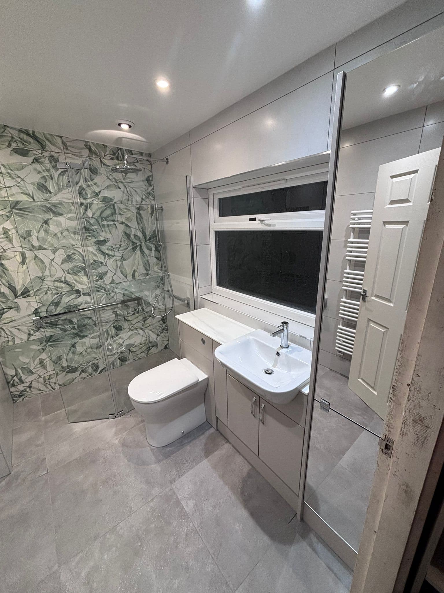 Wet room with botanical shower tiles, wall-hung toilet and marble-topped vanity