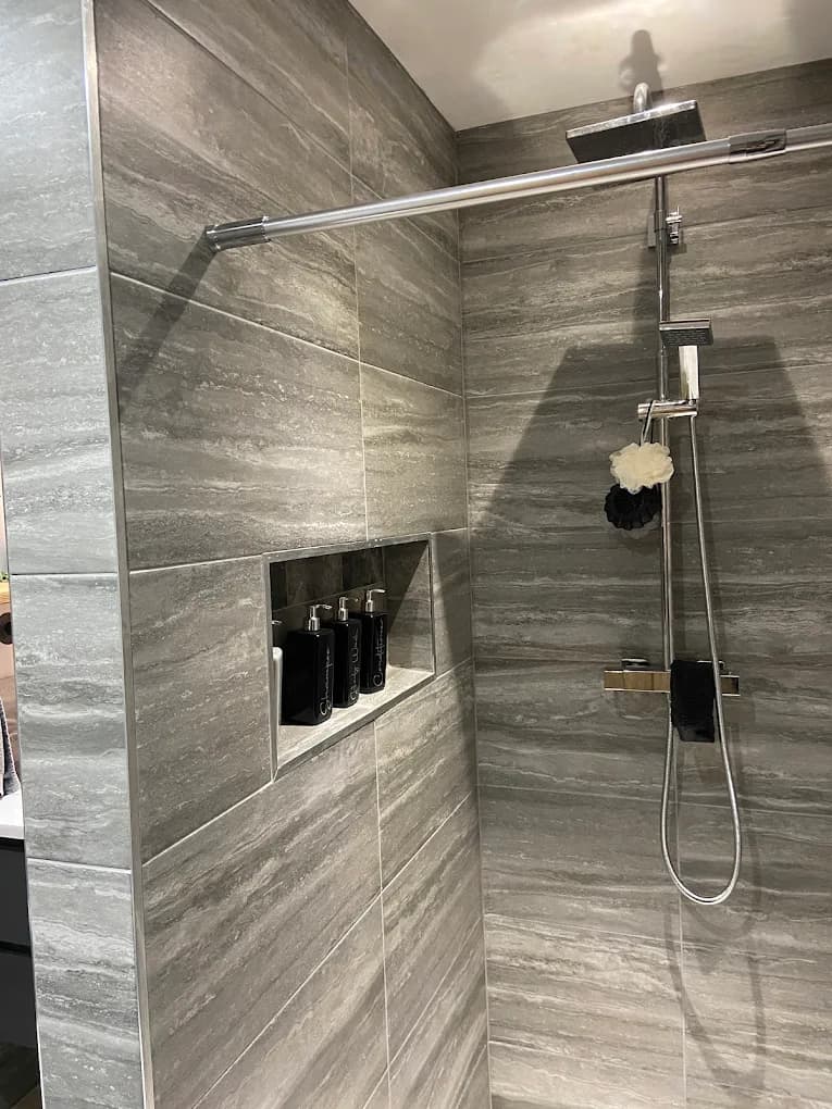 Brushed brass rainfall shower and tiled niche against grey stone-effect tiles