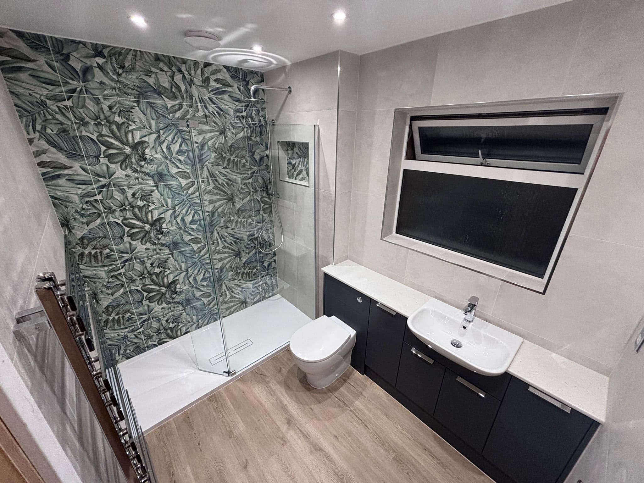 Walk-in shower with bifold glass screen, leaf feature tiles and oak-effect floor