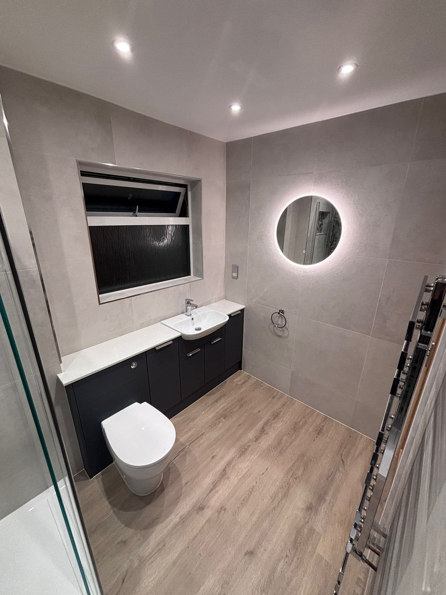 Backlit round LED mirror over a charcoal vanity with a countertop basin