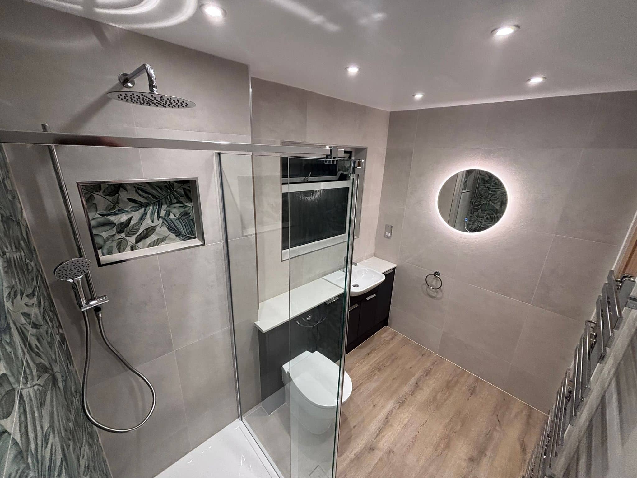 Walk-in shower room with leaf feature tiles, backlit round mirror and charcoal vanity