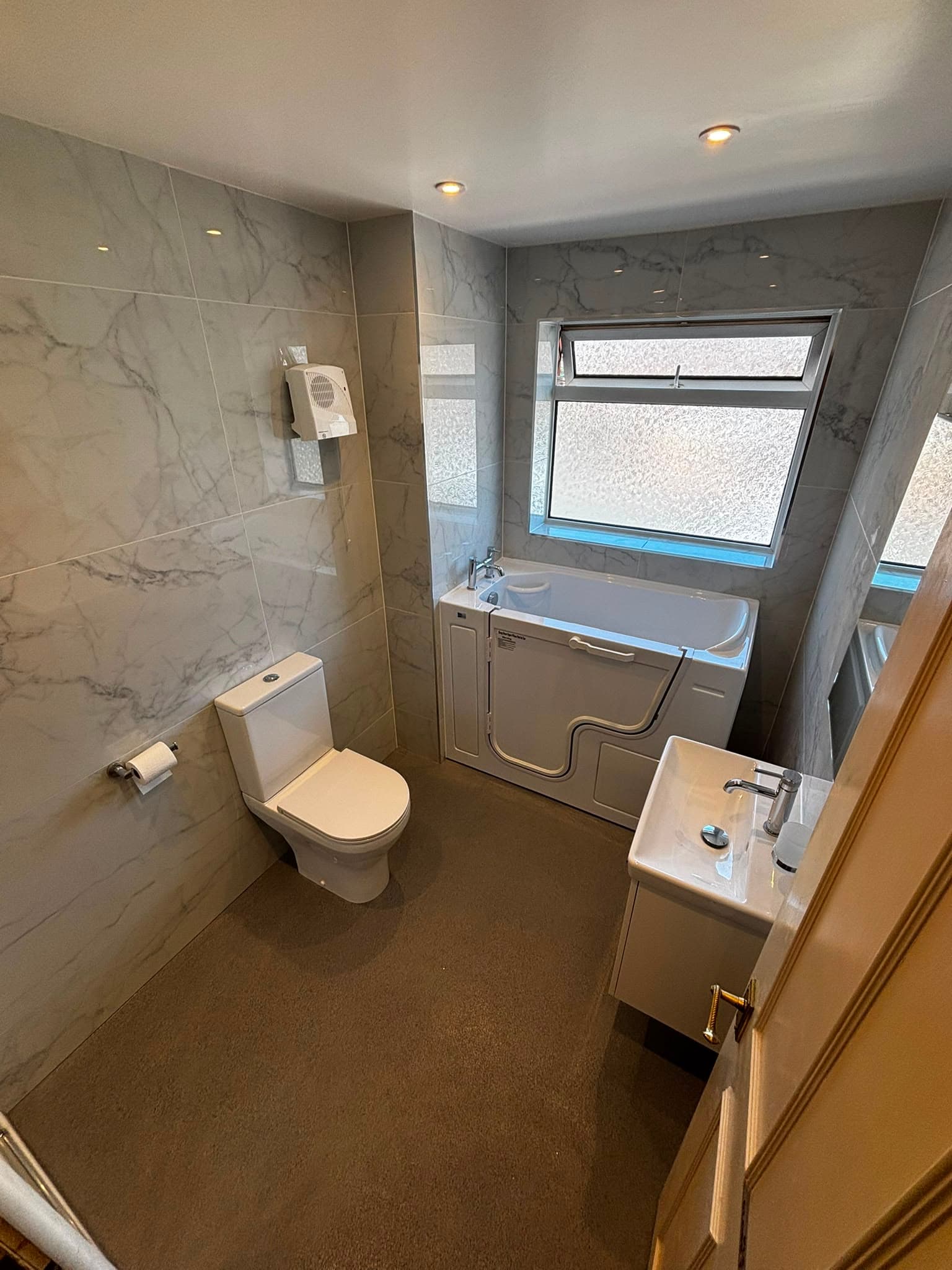 Accessible bathroom with a walk-in bath, marble-effect tiles and wall-hung basin