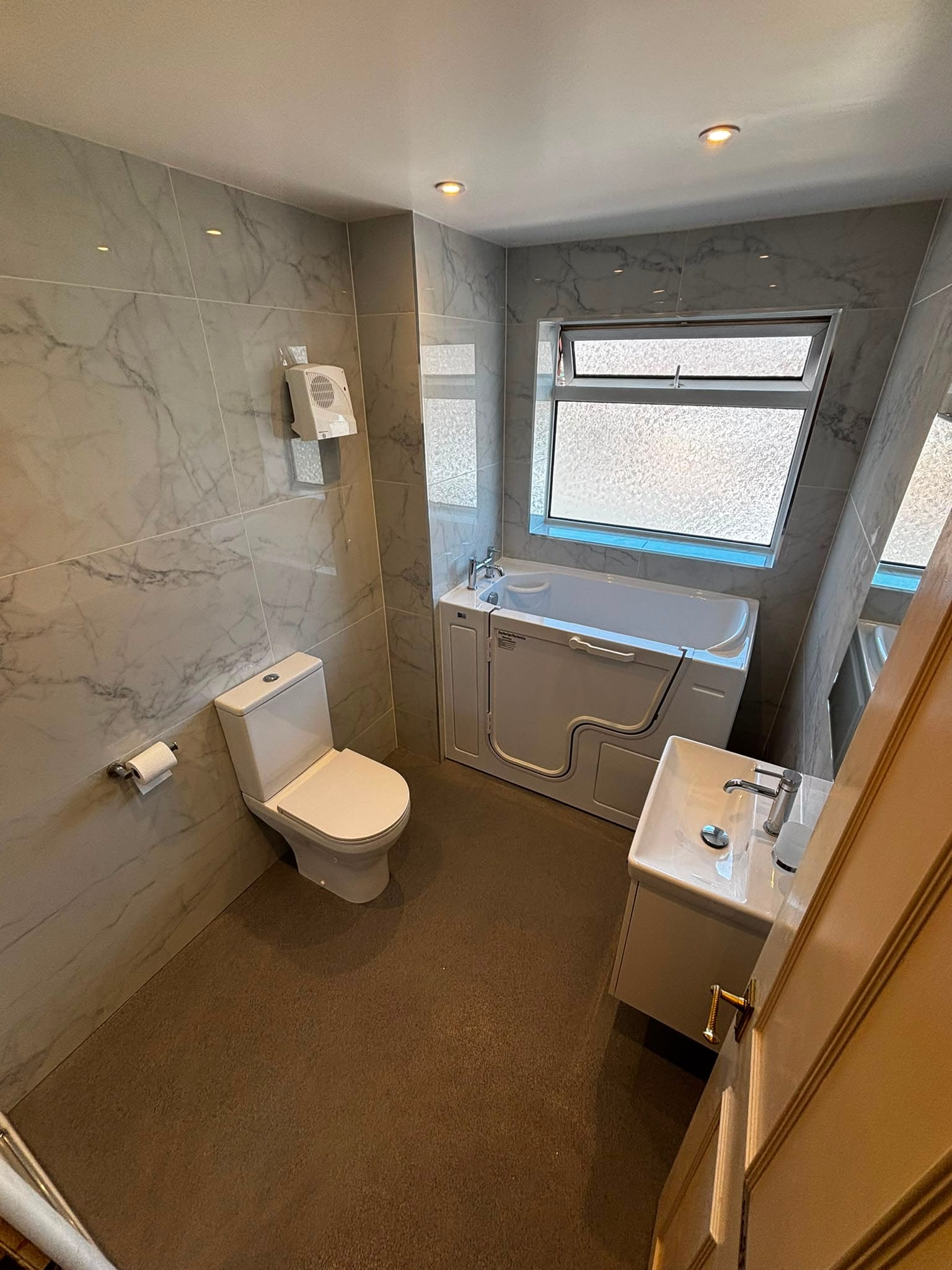 Accessible bathroom with a walk-in bath, marble-effect tiles and wall-hung basin