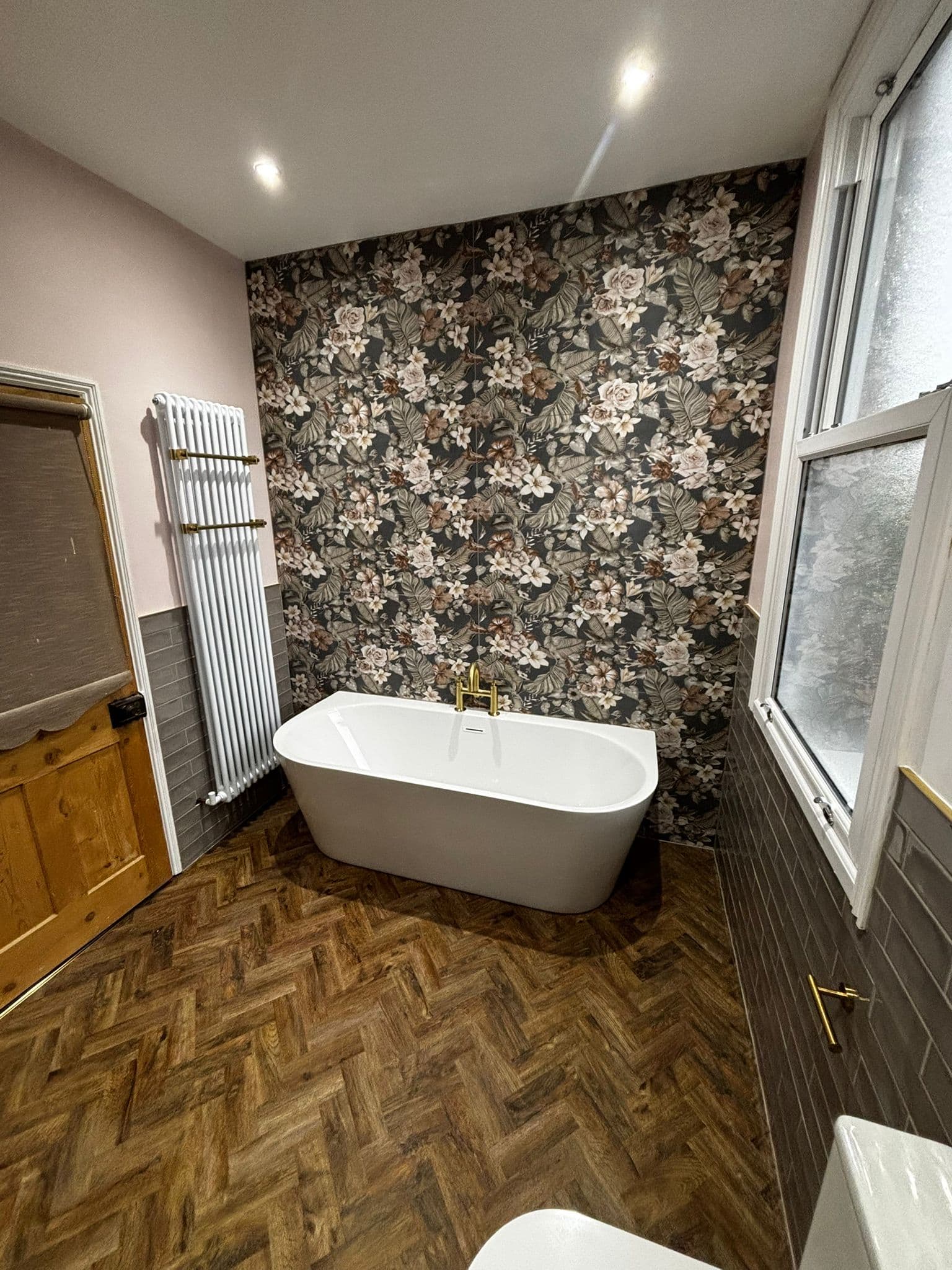 Freestanding oval bath with a gold floor-standing filler against a floral feature wall
