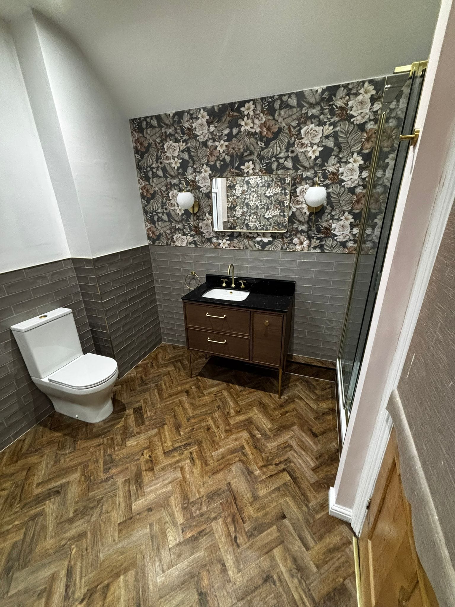 Bathroom with a dark floral feature wall, gold-framed mirror, globe lights and brushed gold brassware