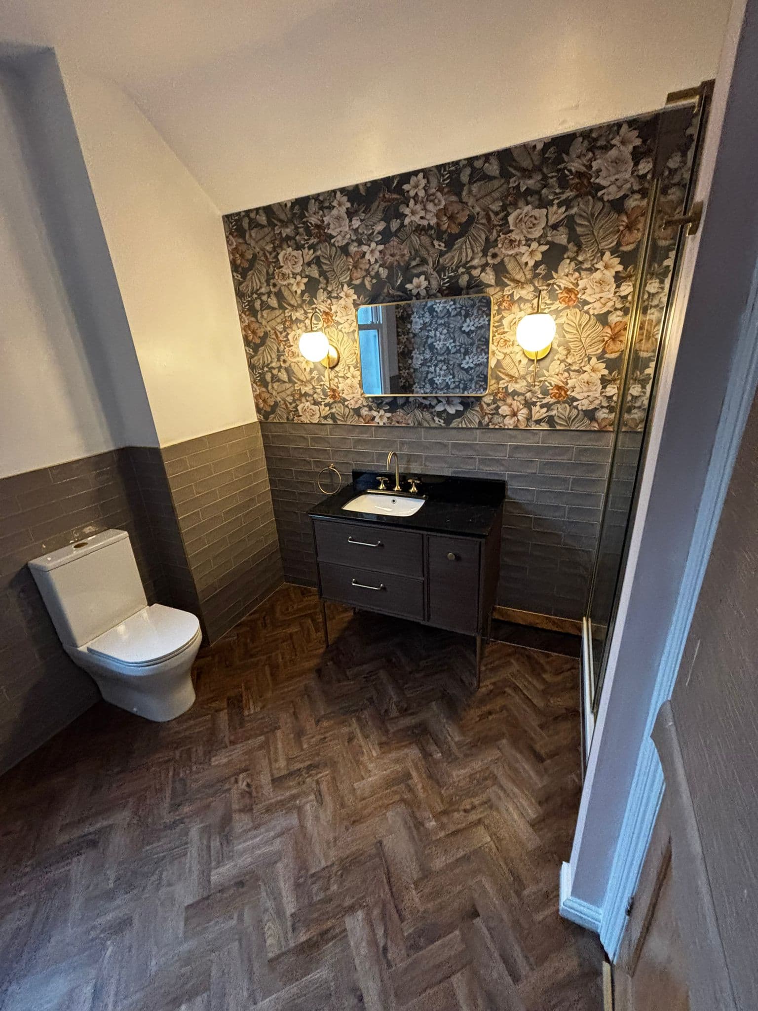 Dark wood vanity with a black marble top, gold tap and lit globe wall lights