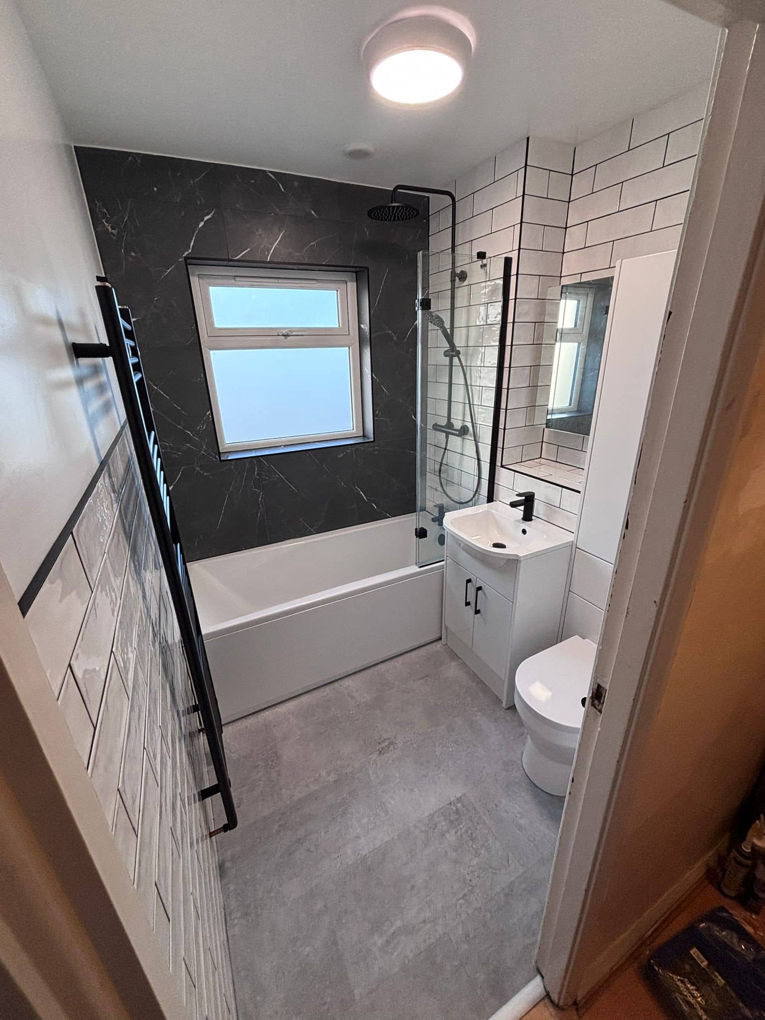 Family bathroom with a black marble feature wall, white metro tiles and matt black shower over the bath