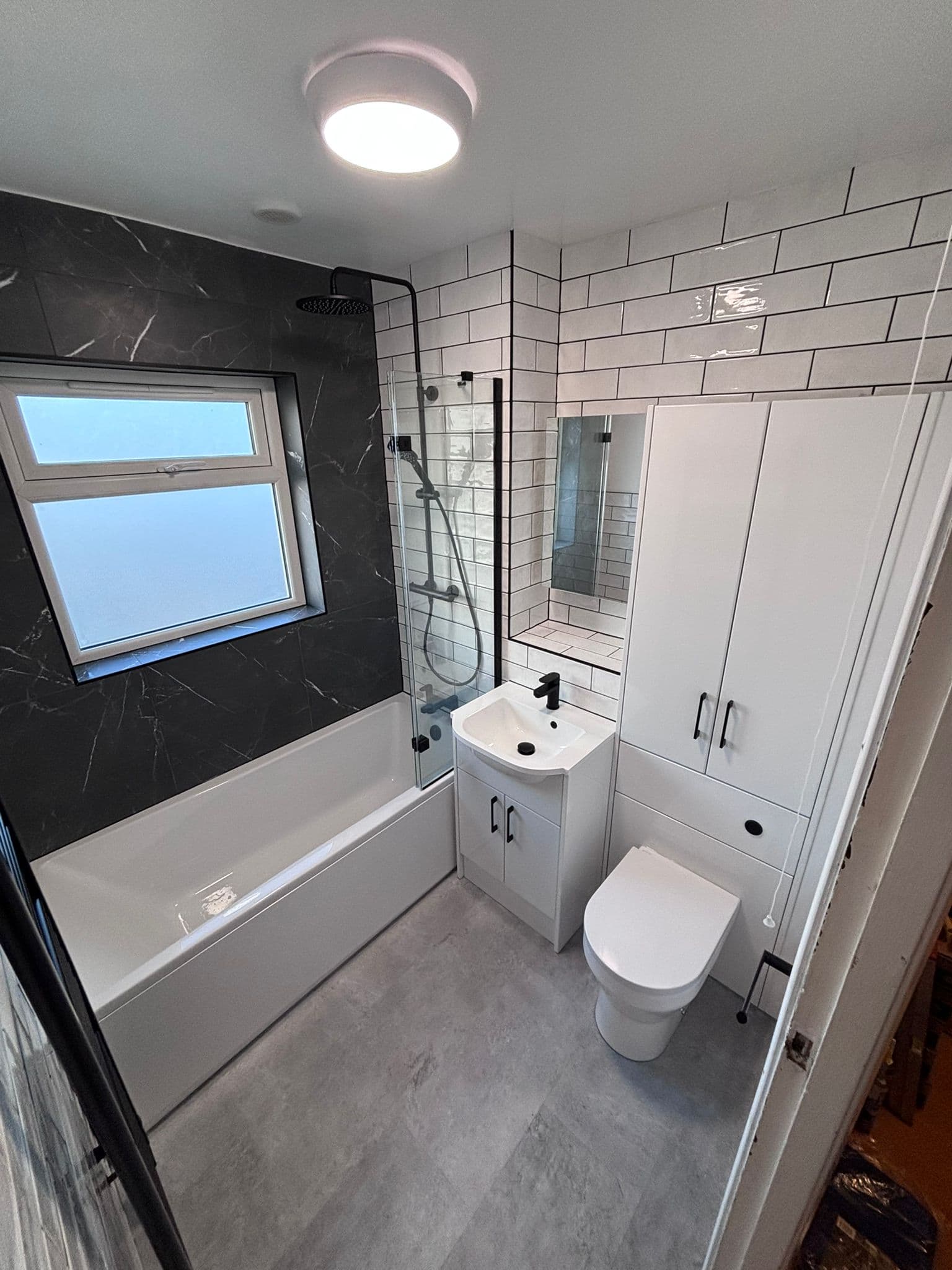 Black marble feature wall and frosted window above the bath with white metro tiles