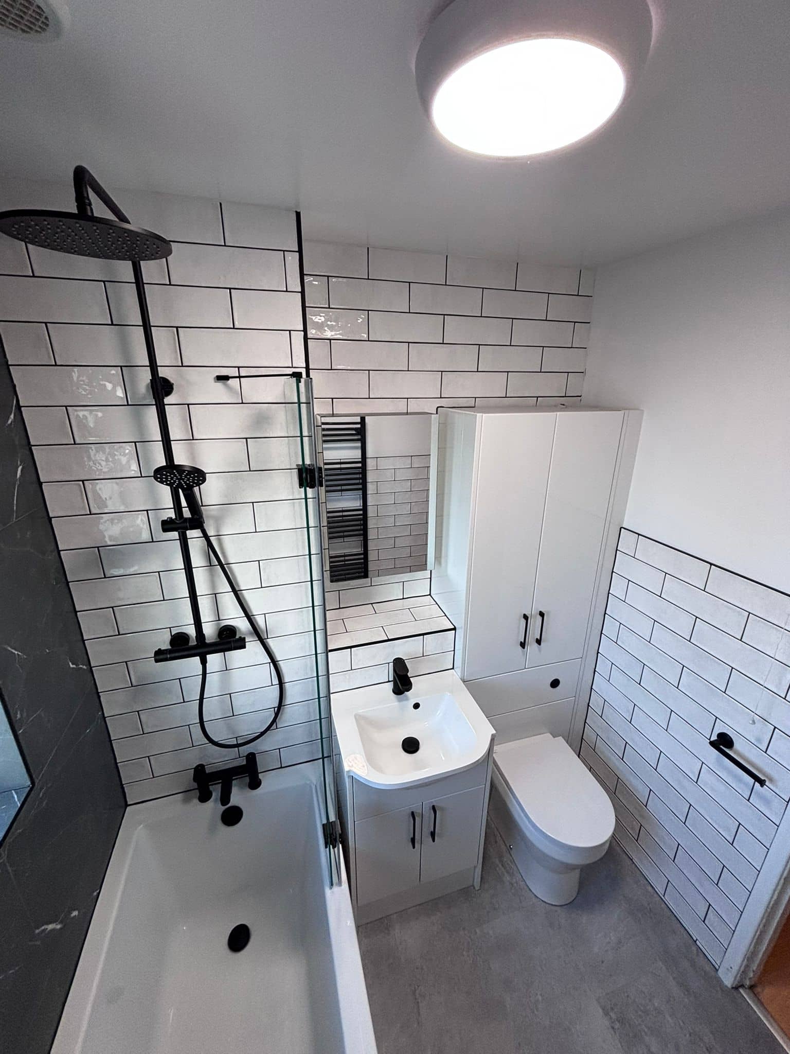 Small bathroom with black rainfall shower, mirror cabinet and tall white storage