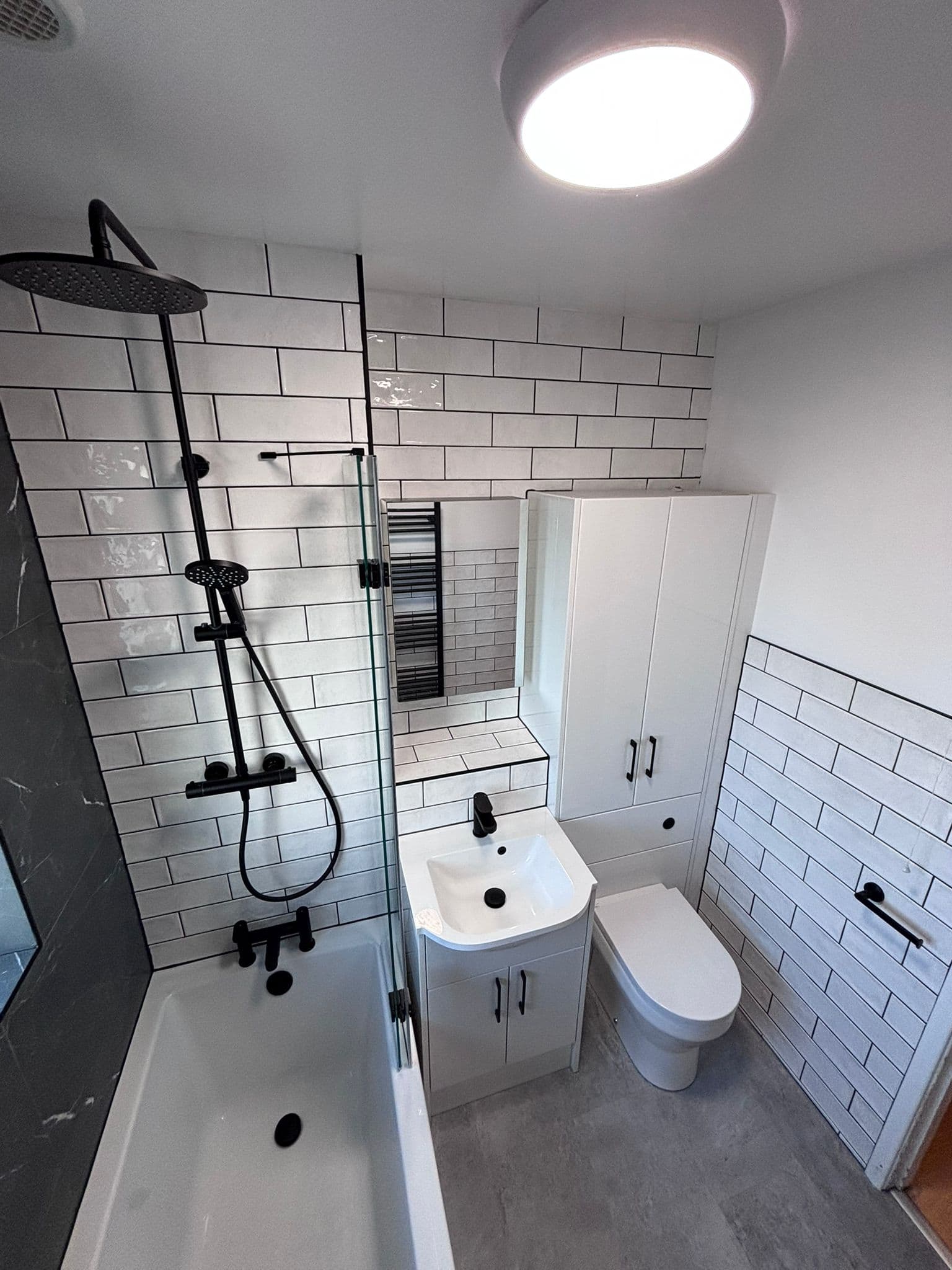 Small bathroom with black rainfall shower, mirror cabinet and tall white storage