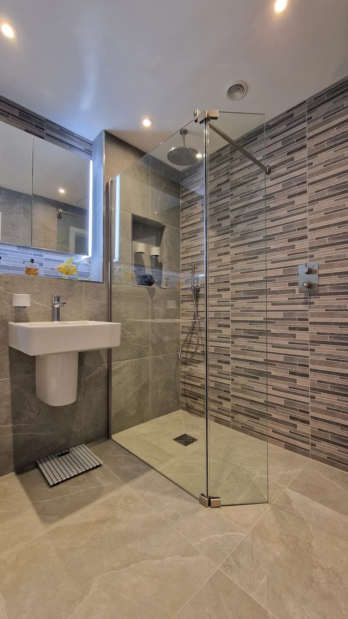 Wet room with a walk-in shower, mosaic feature band, backlit mirror and wall-hung basin