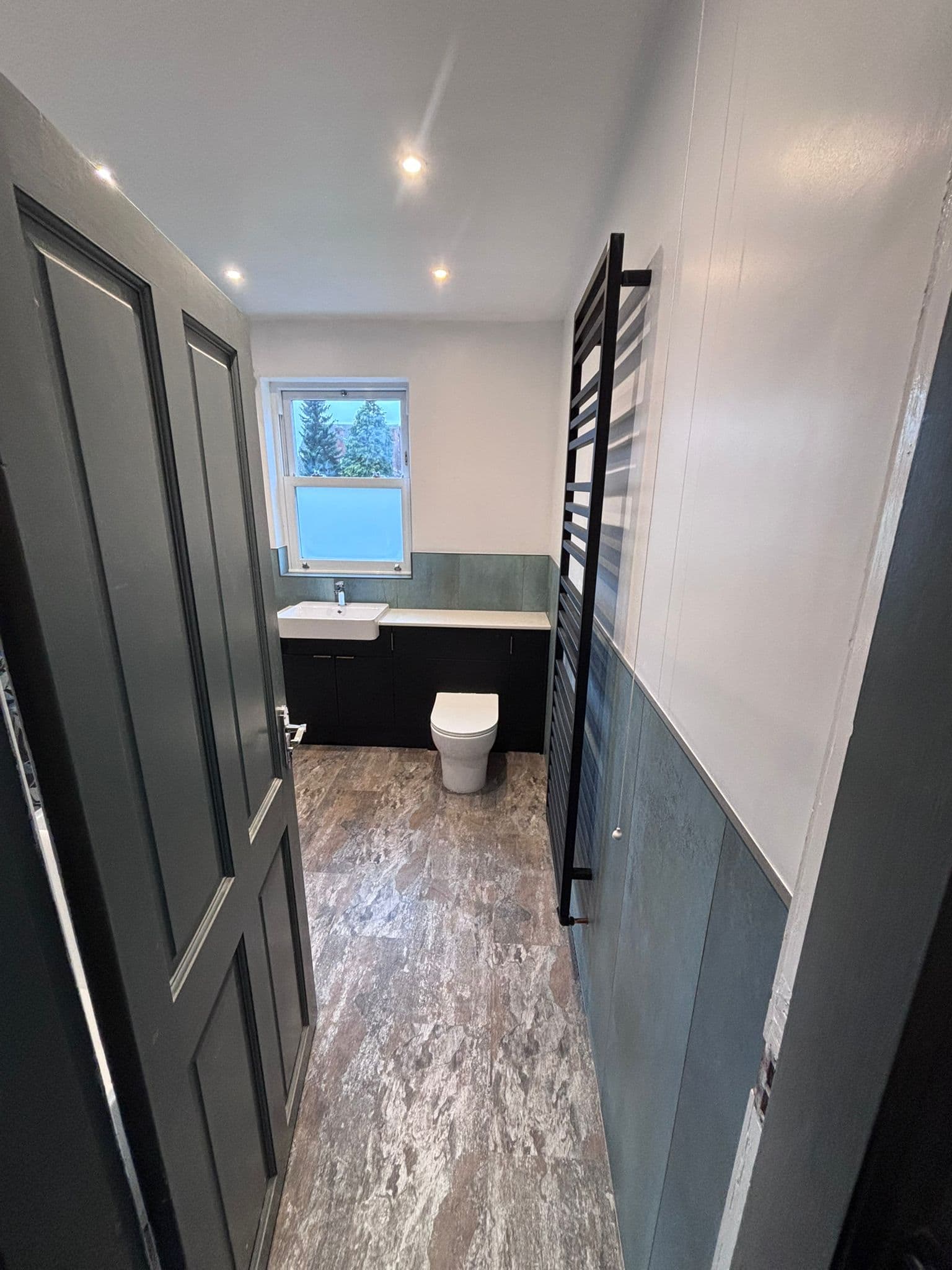 WC area with dark vanity, wall-hung basin, black ladder towel rail and sage tiling