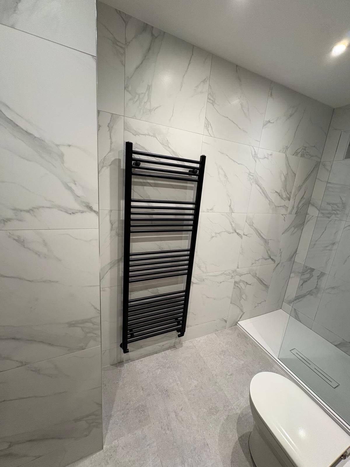 Matt black ladder towel rail against bookmatched marble-effect tiling