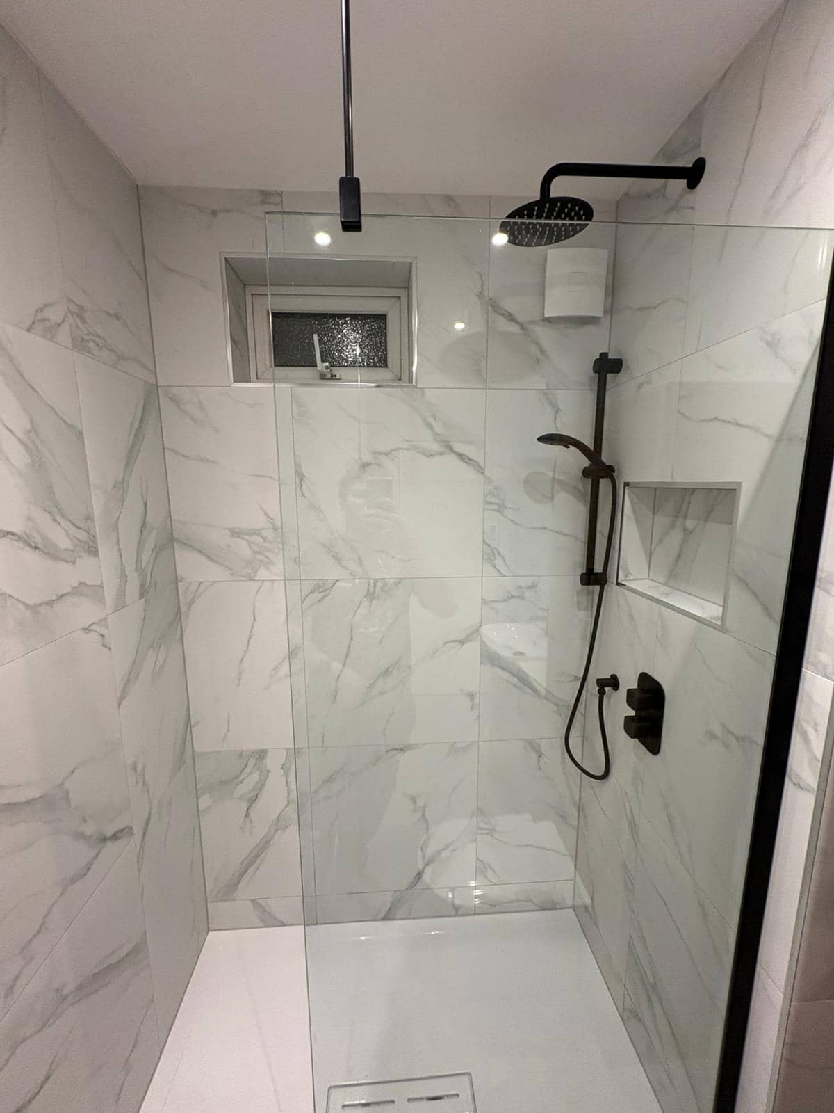 Marble walk-in shower with black rainfall head, tiled niche and linear drain