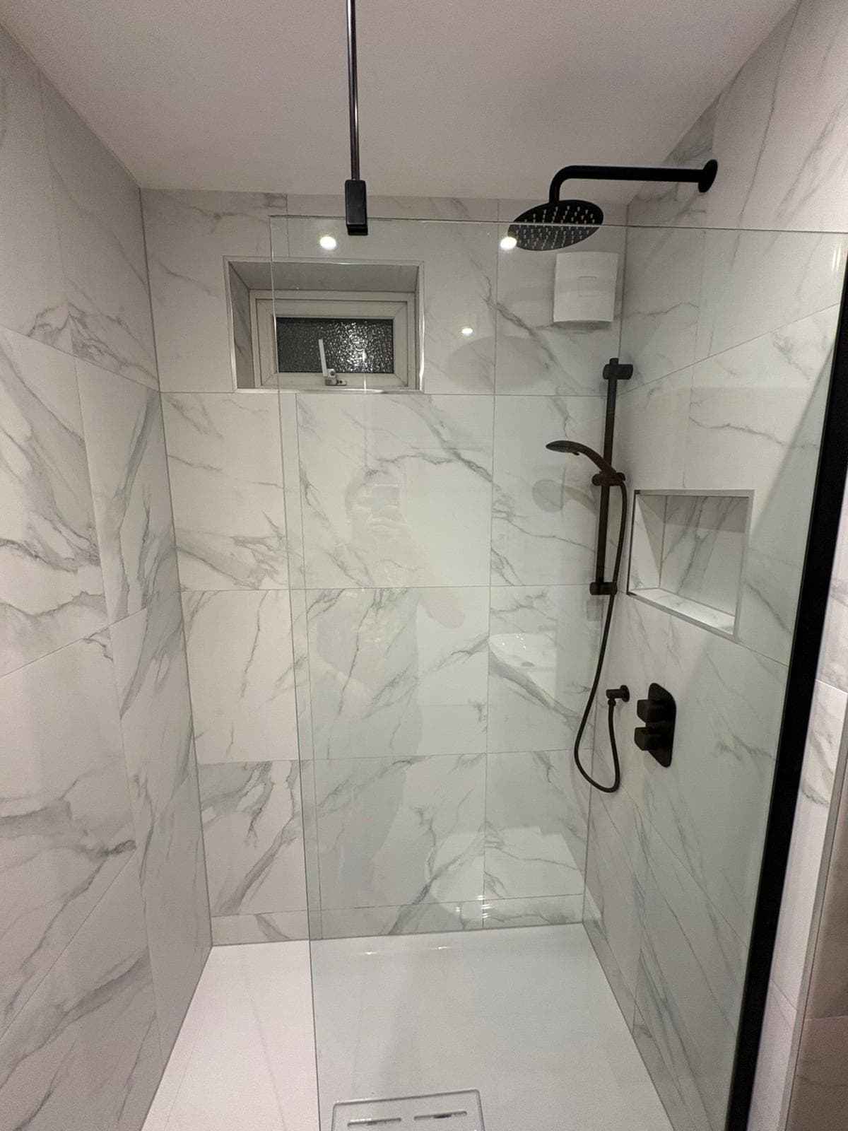 Marble walk-in shower with black rainfall head, tiled niche and linear drain
