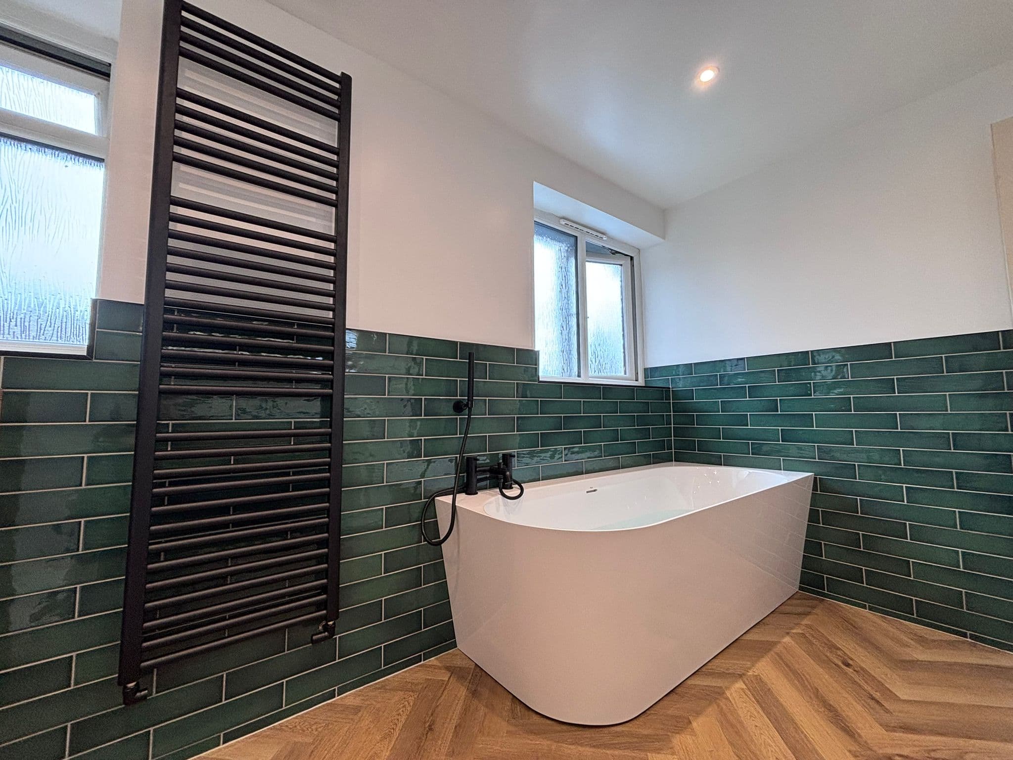 Black floor-mounted mixer tap beside a freestanding bath and green tiles