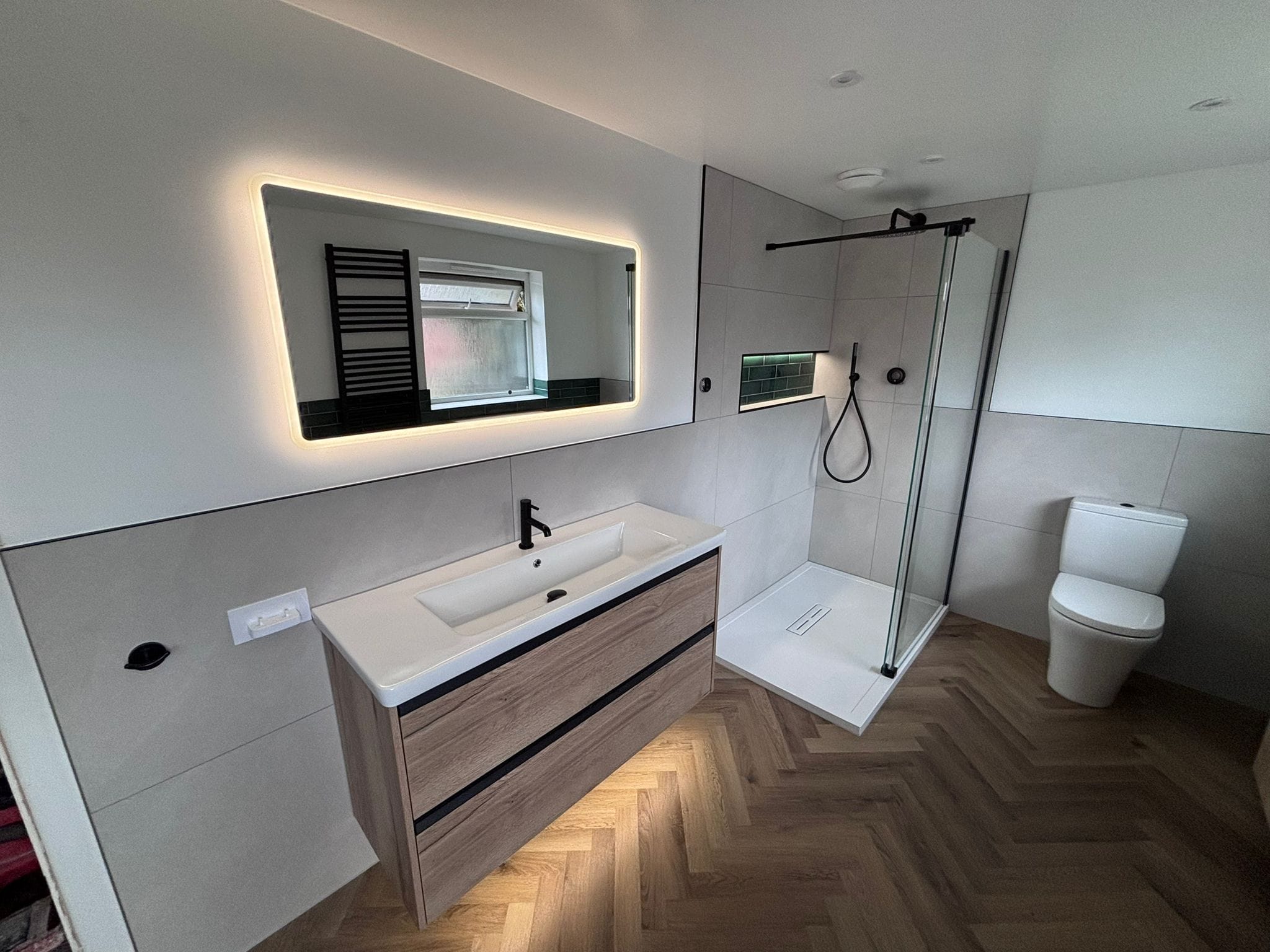 Backlit mirror over an oak vanity with a walk-in shower beyond