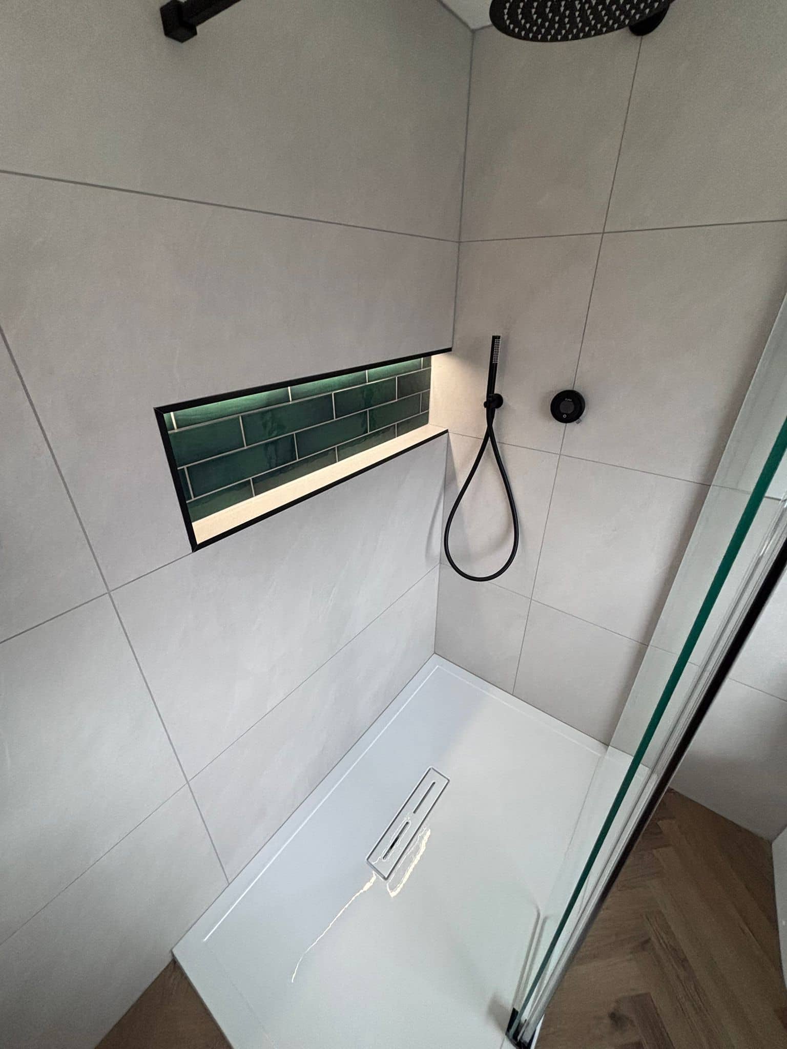 Black rainfall shower beside a green tiled niche with LED strip lighting