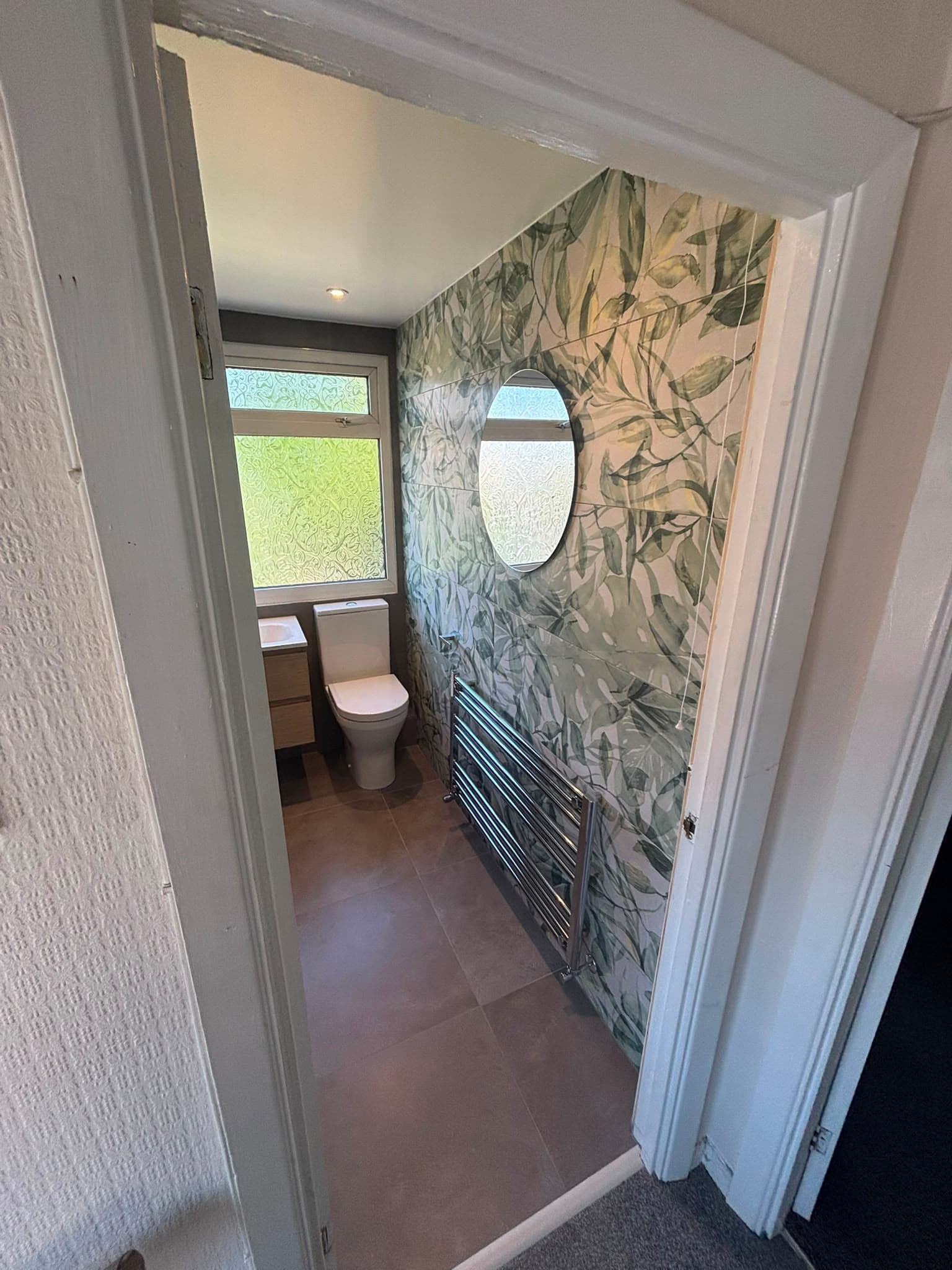 Loft bathroom seen through the door with fern feature wall, toilet and floating vanity