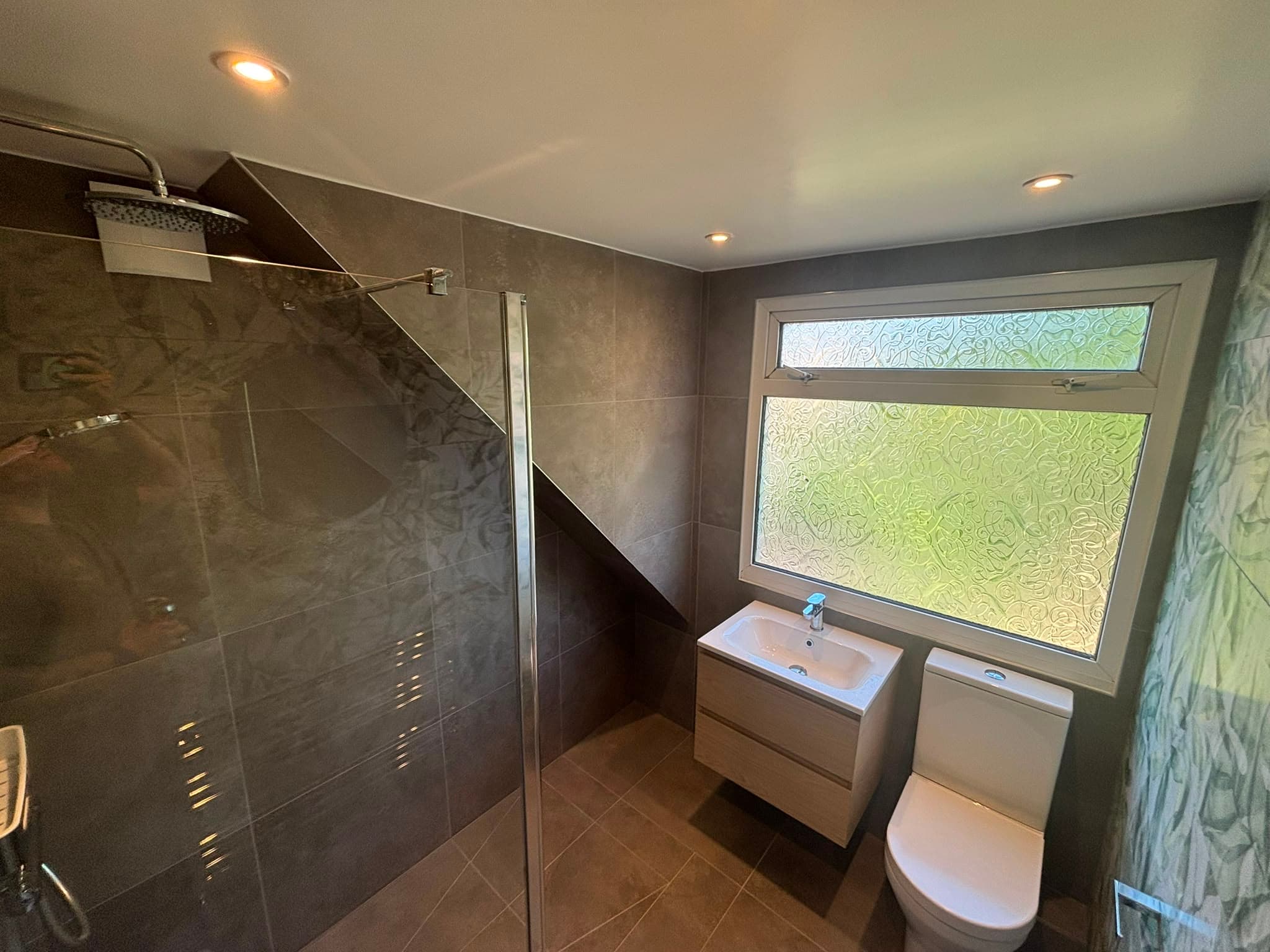 Charcoal-tiled loft wet room with a walk-in glass shower under a sloped ceiling