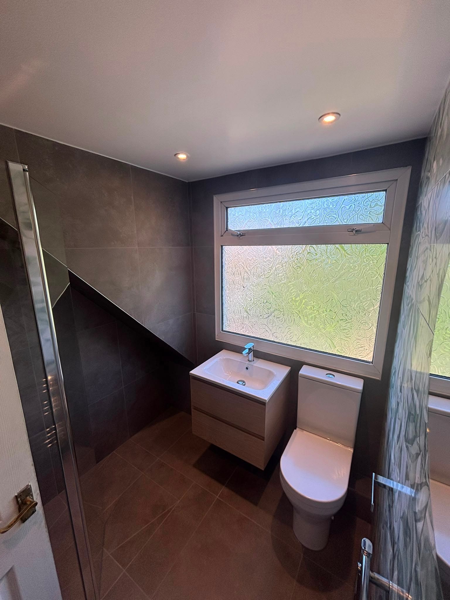Compact loft bathroom with charcoal tiling, a wall-hung basin and a sloped ceiling