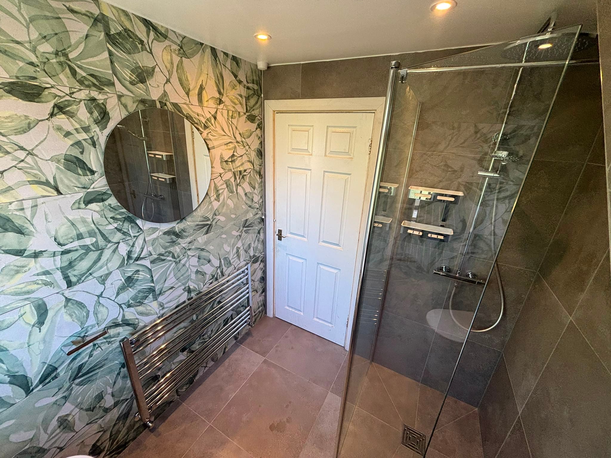 Fern-pattern feature wall with a round mirror and chrome heated towel rail