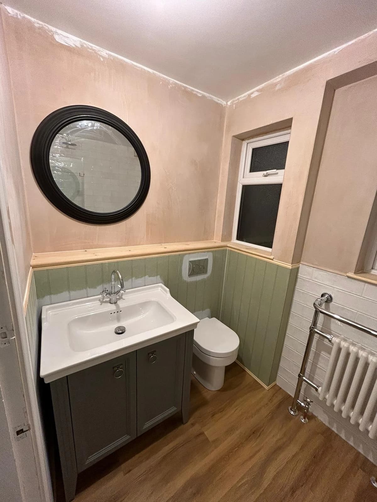 Traditional bathroom with sage half-height panelling, a grey vanity and a round black-framed mirror