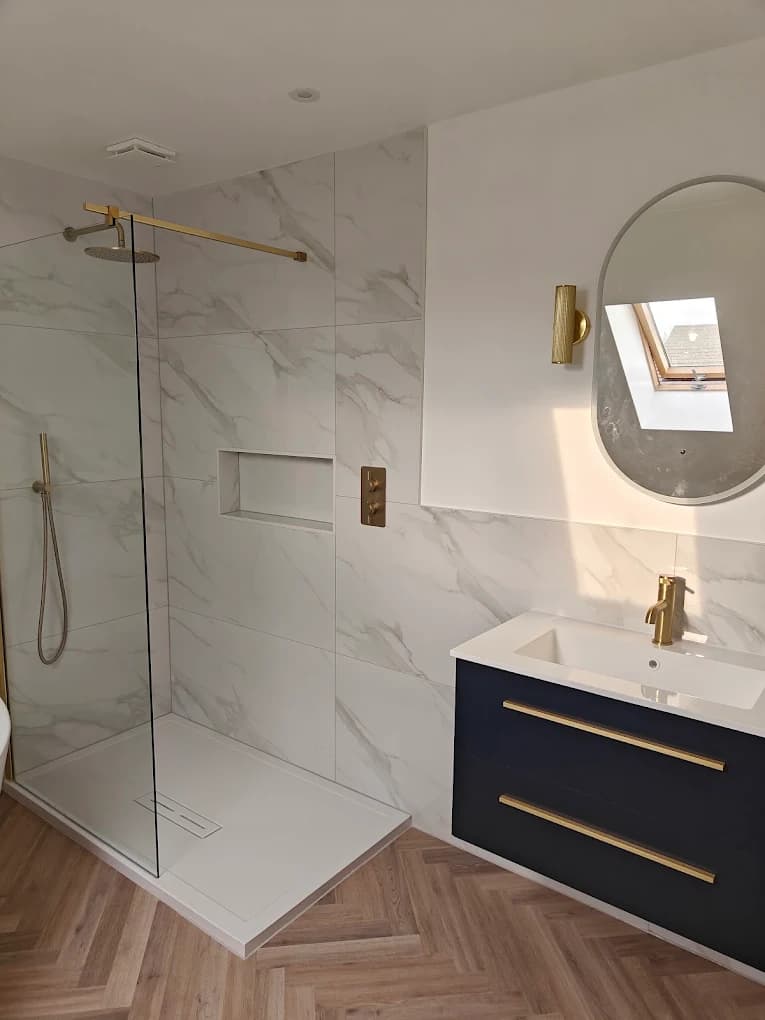 Marble walk-in shower with brushed gold brassware beside a navy vanity with gold handles