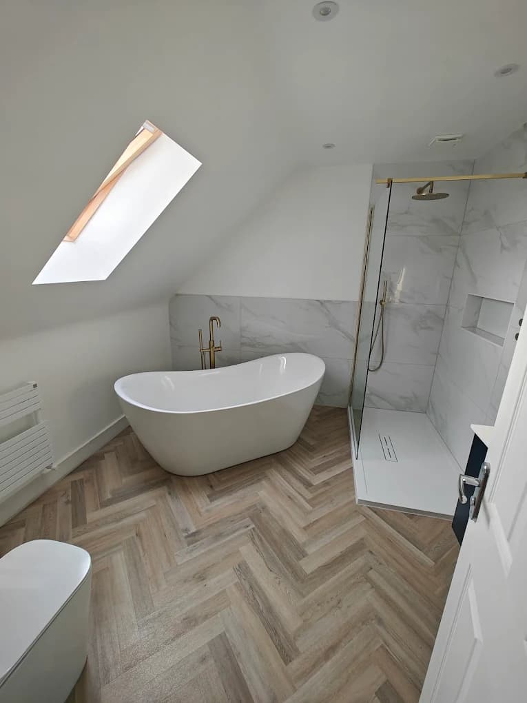 Freestanding bath under a loft skylight with a herringbone floor and gold floor-standing filler