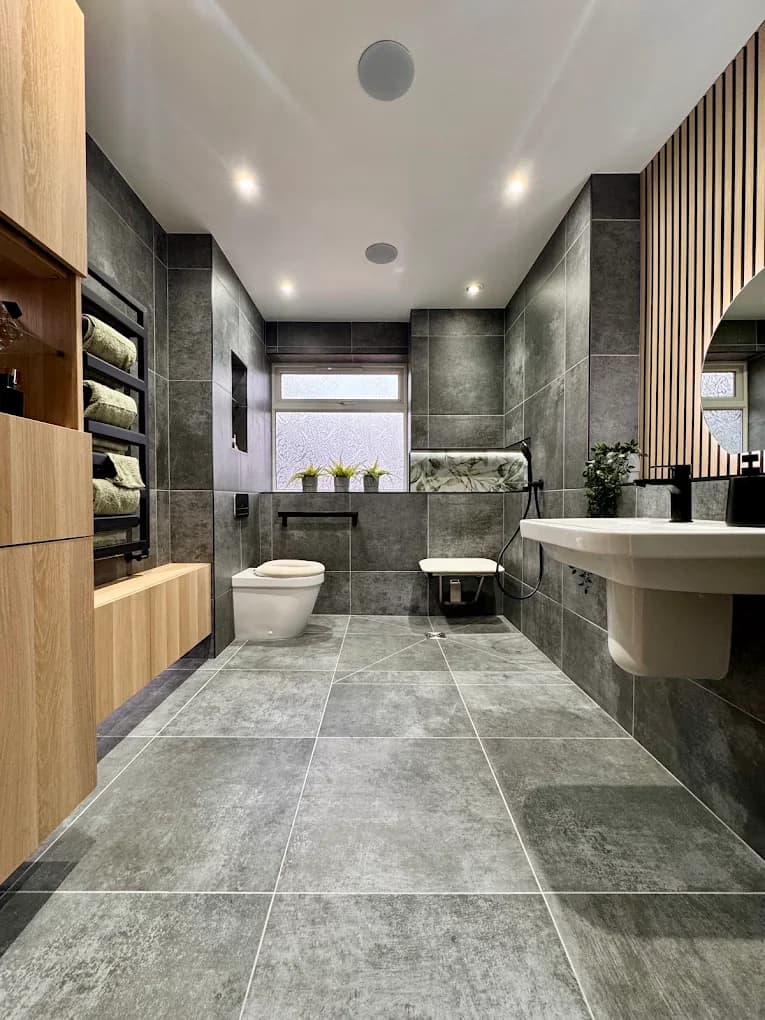 Spacious grey bathroom with an oak slat wall, fold-down shower seat, wall-hung toilet and large-format tiles