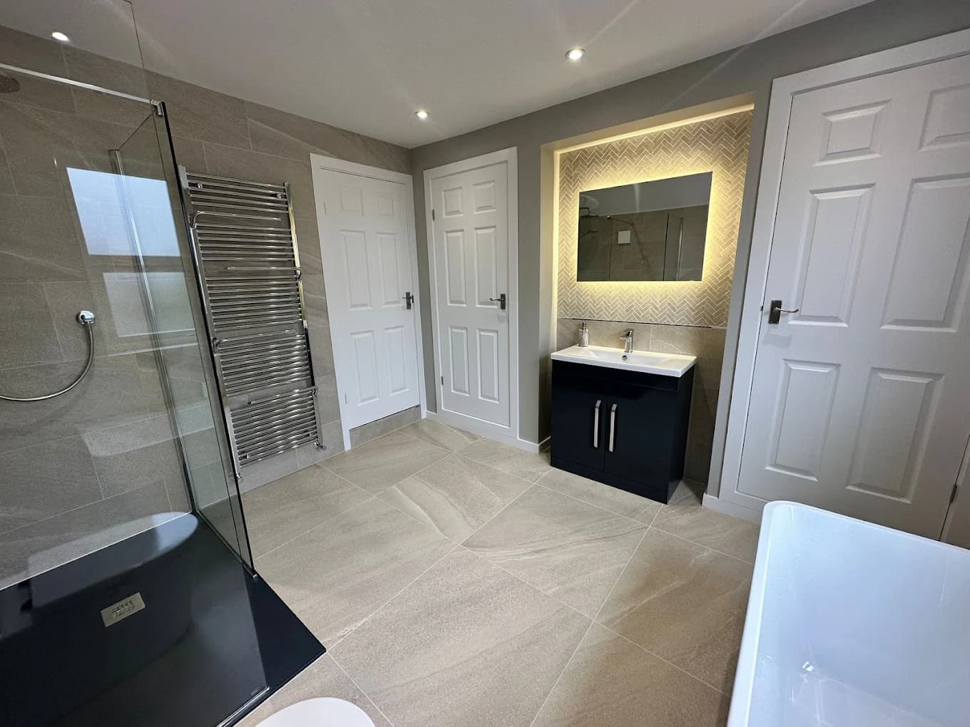 Shower room with a black slate-effect tray, navy vanity and warm backlit mirror