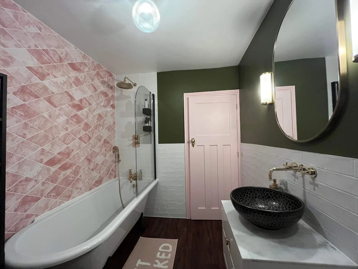 Bathroom with a pink marble feature wall, sage walls, freestanding bath and black vessel basin