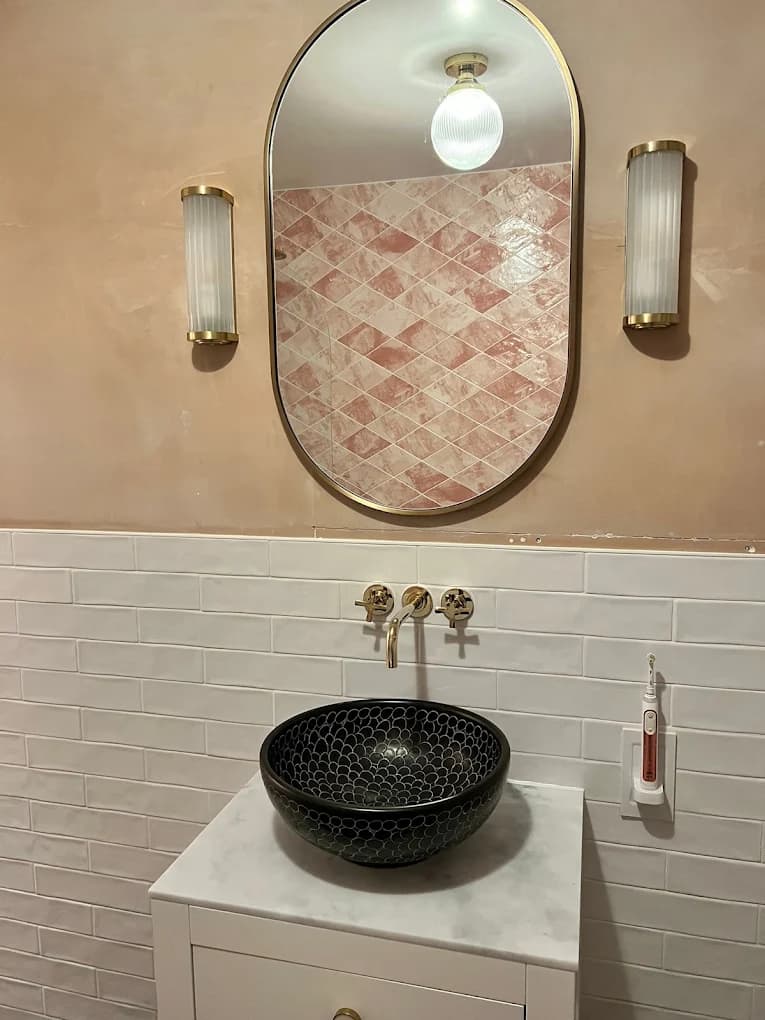 Black vessel basin and gold taps under an oval mirror against pink marble tiles