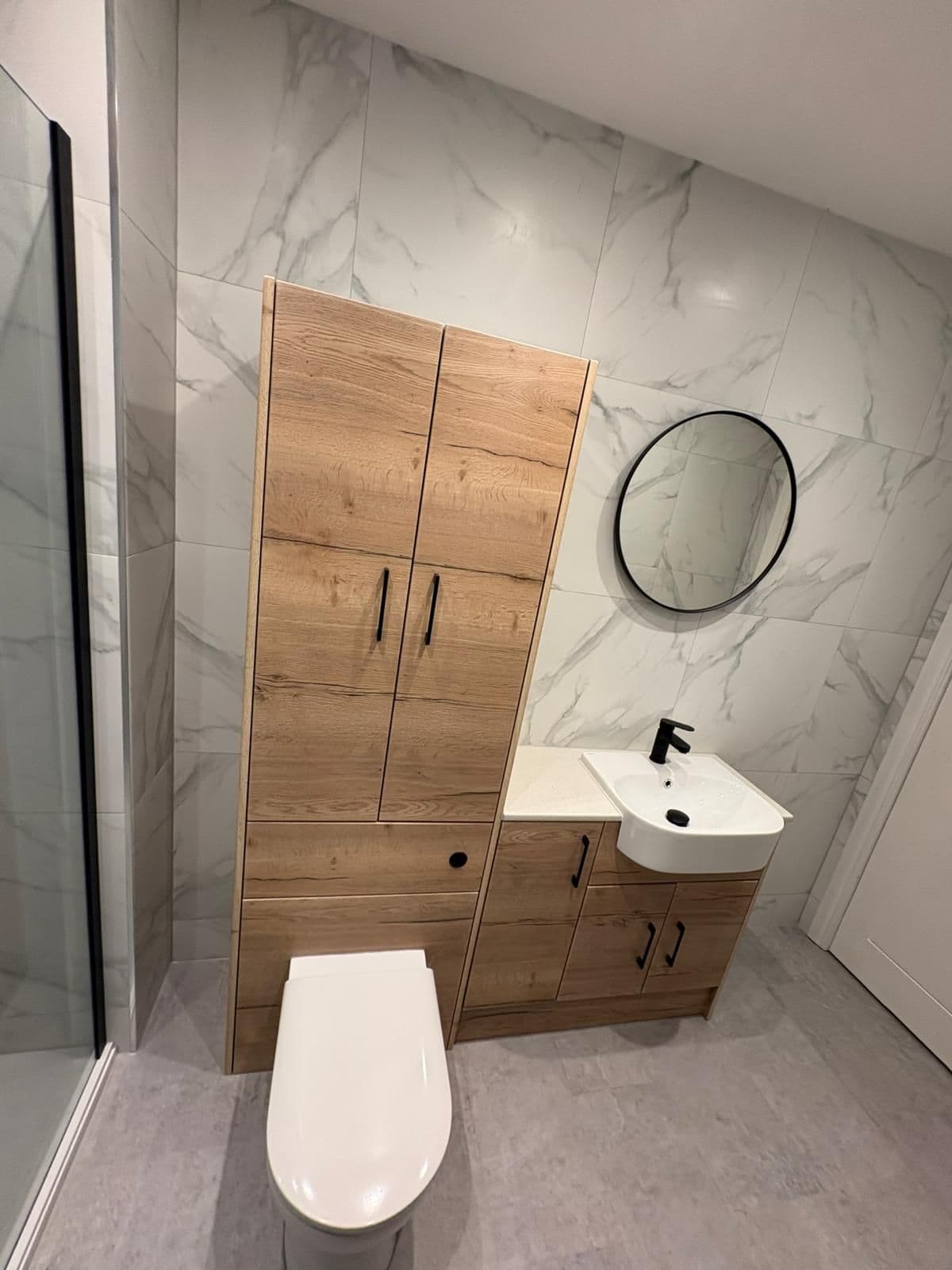 Marble-effect shower room with oak-effect furniture, a round black mirror and black brassware