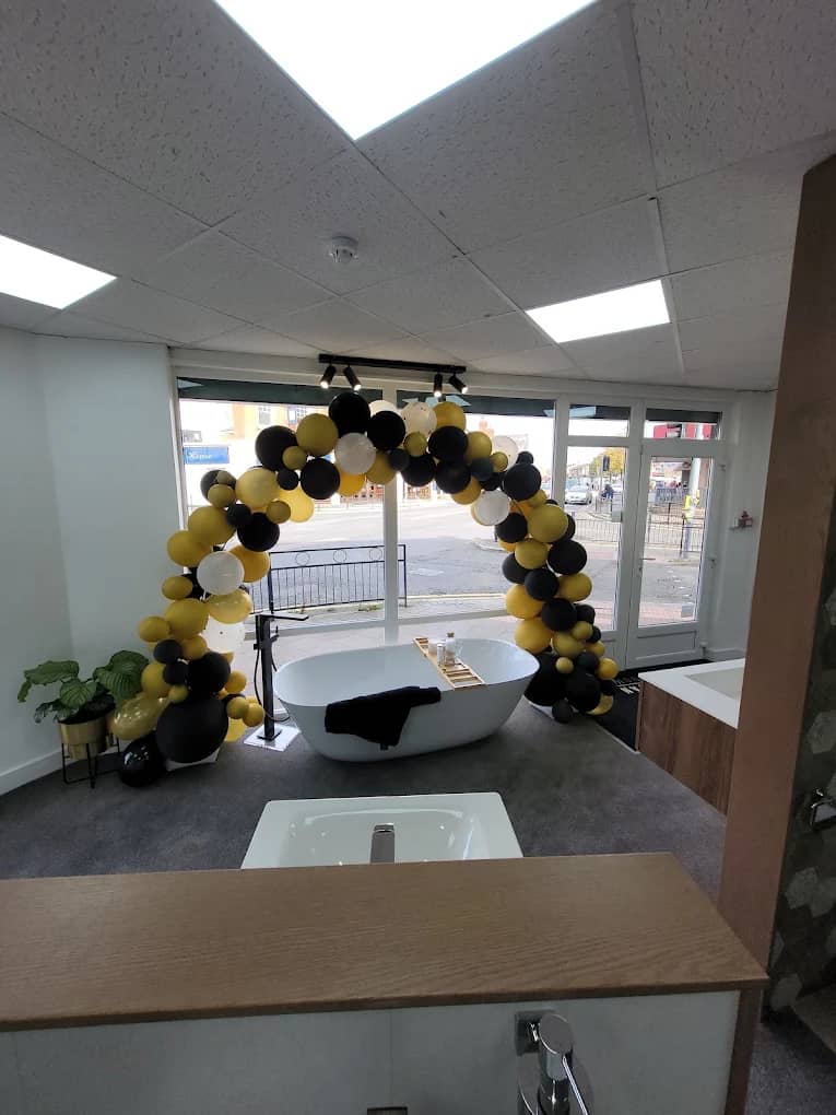 Black and gold balloon arch over a freestanding bath display in the showroom