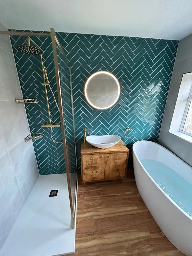 Teal herringbone feature wall behind a freestanding bath with a wood vanity and brushed gold fittings